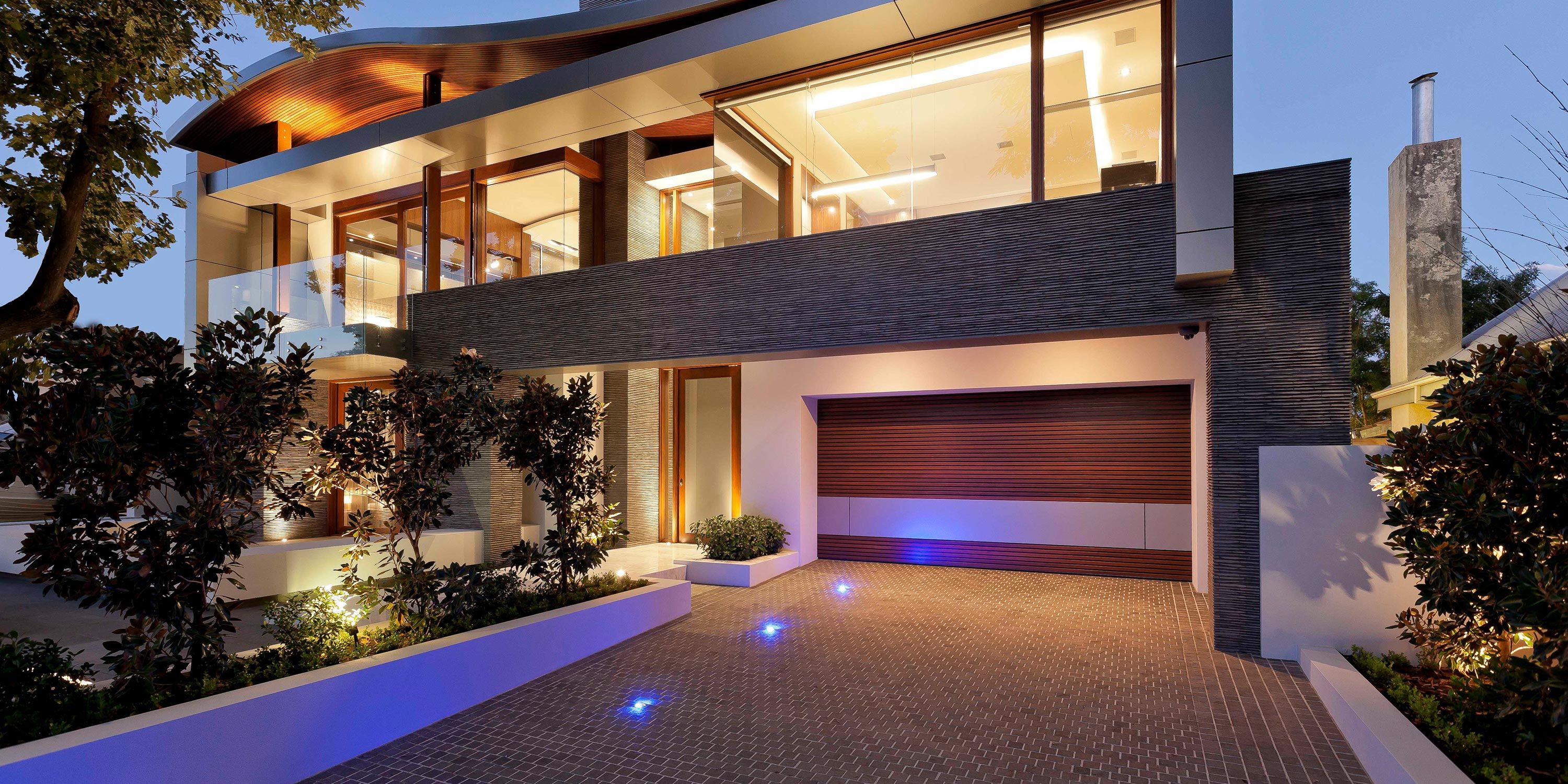 A modern two-story home with a paved driveway, featuring a sleek garage and evening lighting.