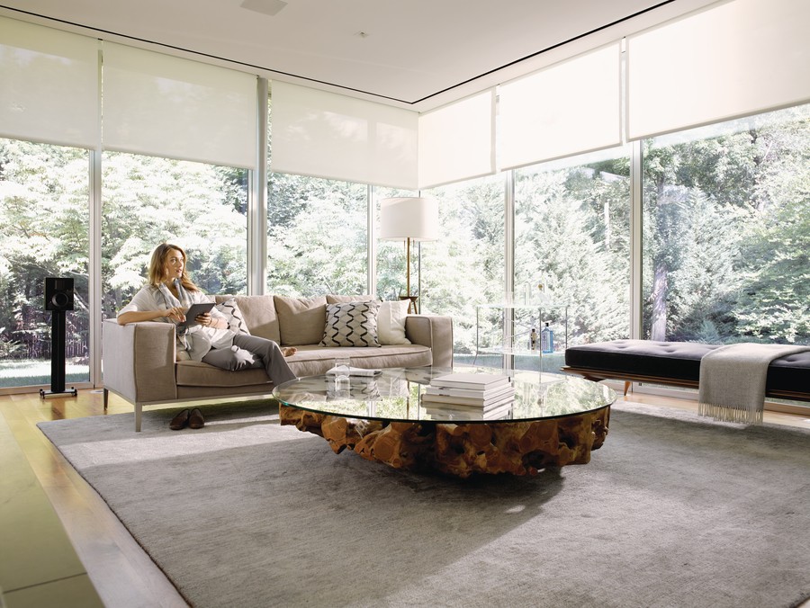 A modern living room in Whitefish featuring elegant motorized shades, offering a view of lush greenery.