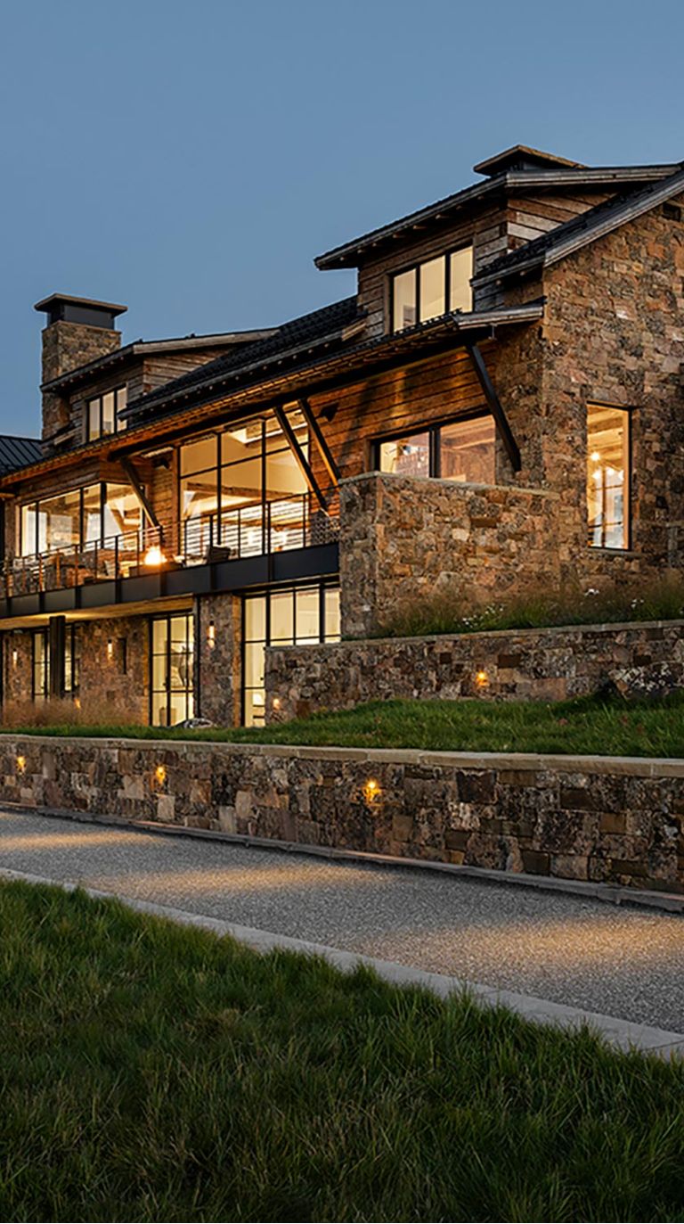 Exterior of a stone and wood house with illuminated path at dusk