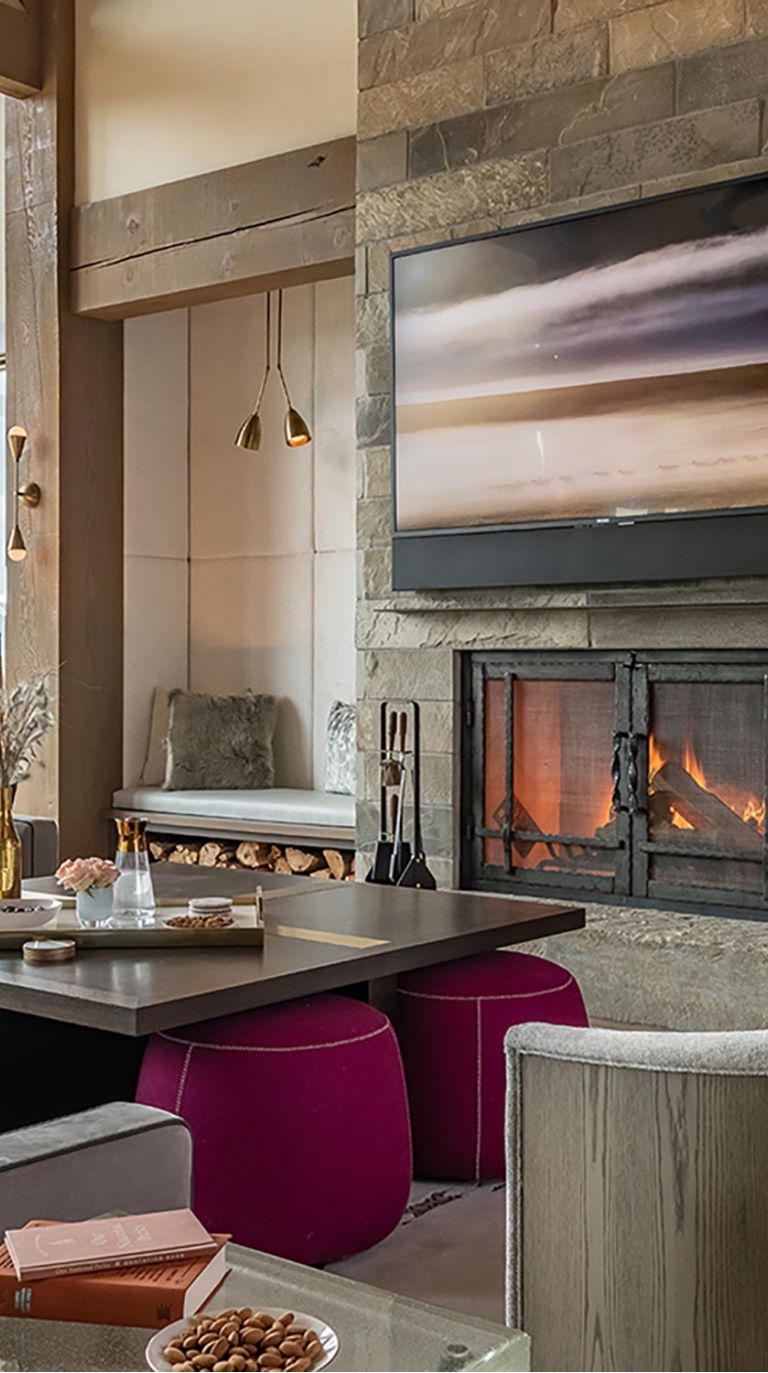 Living room with a television mounted above a stone fireplace and colorful ottomans